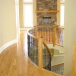 Rich, golden, solid hardwood flooring by Meistercraft complements the stone fireplace, rounded stair and wrought iron railing in this modern home