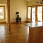Rich hardwood flooring by Meistercraft Wood Flooing complements the cast iron woodstove and kitchen cabinets in this rustic cottage
