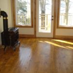 Rich and lustrous hardwood floor by Meistercraft Wood Flooing adds complements the cast iron woodstove in this rustic cottage overlooking the grounds and lake