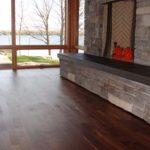 Custom hardwood flooring by Meistercraft complements this massive stone fireplace and glass wall overlooking the grounds and lake beyond