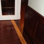 Elegant custom inlay sets off the beauty of dark wall wainscot panels; custom flooring by Meistercraft Wood Flooring