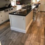 Gray hardwood complements off-white cupboards in this modern open concept kitchen; custom hardwood floor by Meistercraft Wood Flooring