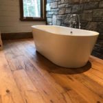Rich solid wood flooring complements the wood and stone walls & soaker tub in this rustic bathroom; custom flooring by Meistercraft Wood Flooring