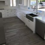 Gray hardwood flooring complements the white cupboards in this modern open concept kitchen; custom hardwood floor by Meistercraft Wood Flooring