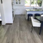 Gray hardwood flooring complements the white cupboards in this modern open concept kitchen; custom hardwood floor by Meistercraft Wood Flooring