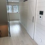 Light coloured hardwood complements the wood walls and sliding door in this rustic hallway - custom hardwood floor by Meistercraft Wood Flooring