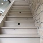 Light coloured hardwood stairs complement limestone wall; custom hardwood flooring by Meistercraft