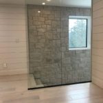 Light coloured hardwood complements this glass divider, limestone and wood walls; custom hardwood by Meistercraft Wood Flooring